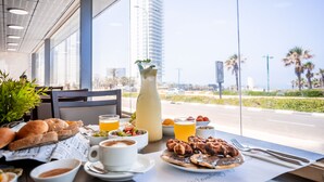 A breakfast table with various dishes, a pitcher, and a view of a tall building and palm trees.
