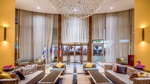 A lobby with a large chandelier, patterned sofas, and a view of the outside through large windows.