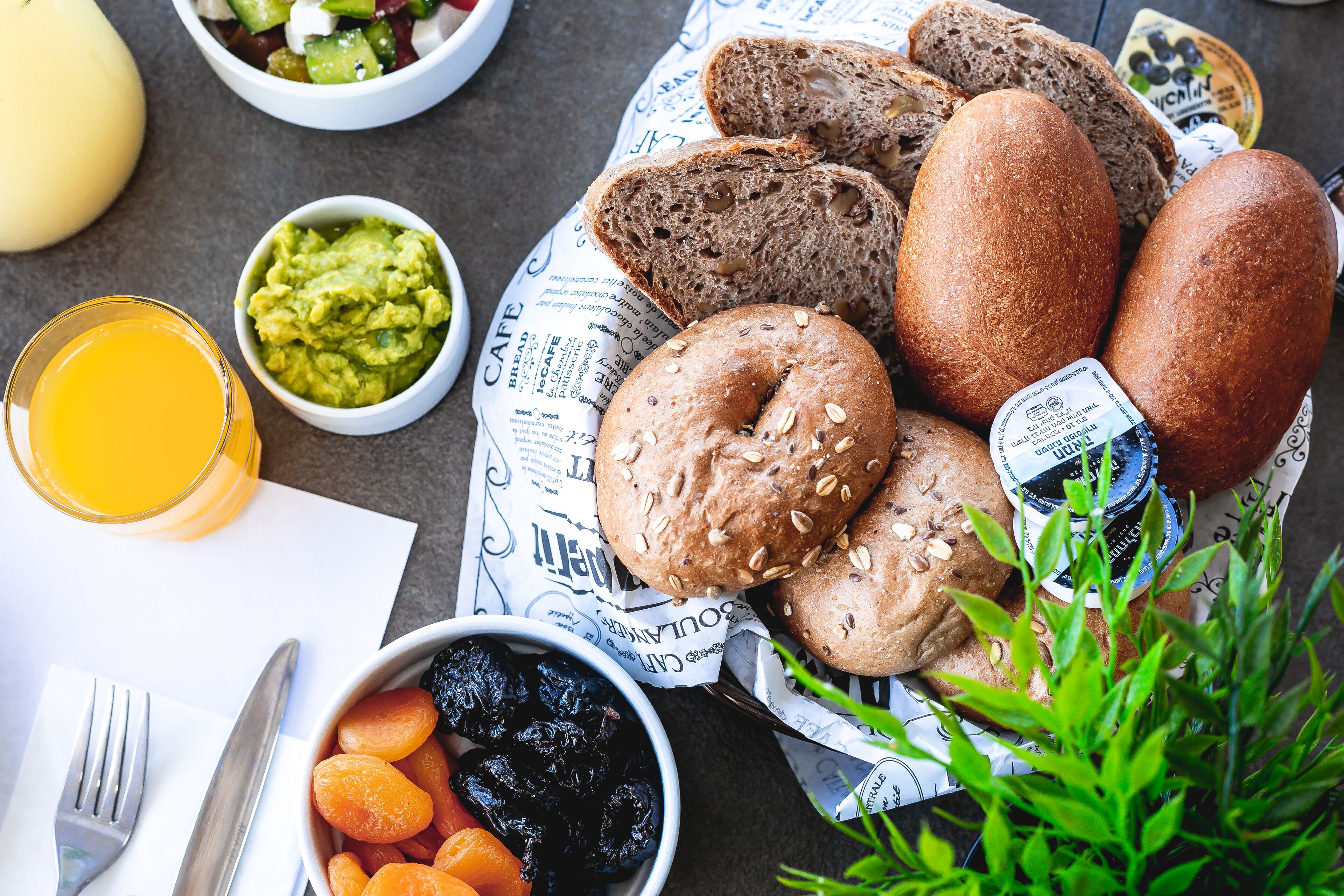 Ein Frühstückstisch mit Brot, einer Schüssel Datteln, einem Glas Orangensaft und einer Guacamole-Schale.