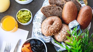Ein Frühstückstisch mit Brot, einer Schüssel Datteln, einem Glas Orangensaft und einer Guacamole-Schale.