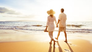 A couple walking on a beach with the ocean in the background.