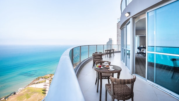 A balcony with wicker furniture, a dining table, and a view of the ocean.