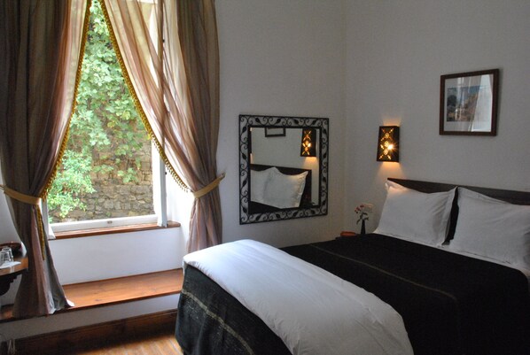 A bedroom with a bed, a window with curtains, a mirror, and a wall-mounted light fixture. - Dar El Kasbah (Tangier)