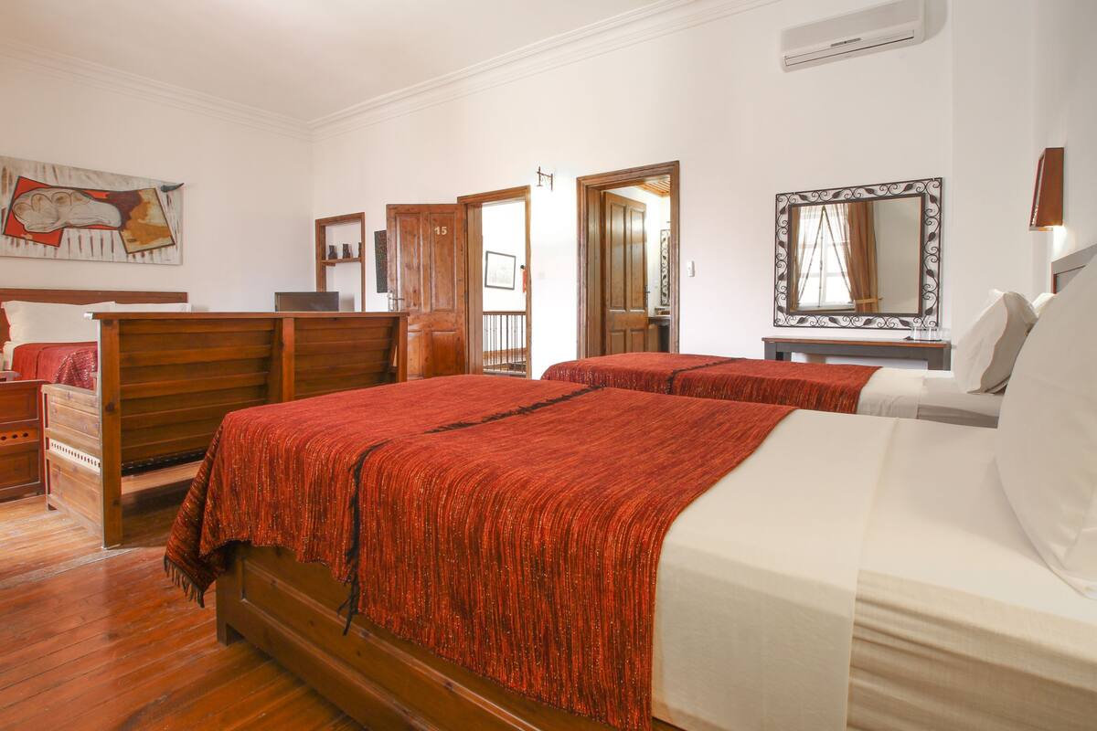 A hotel room with two beds, wooden headboards, a large mirror, and a painting on the wall.