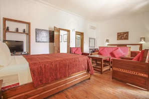 A hotel room with a bed, a TV, a wooden dresser, a red sofa, and a wooden table. - Dar El Kasbah (Tangier)