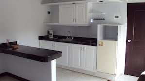 Una cocina con armarios blancos, encimera negra, fregadero y refrigerador.