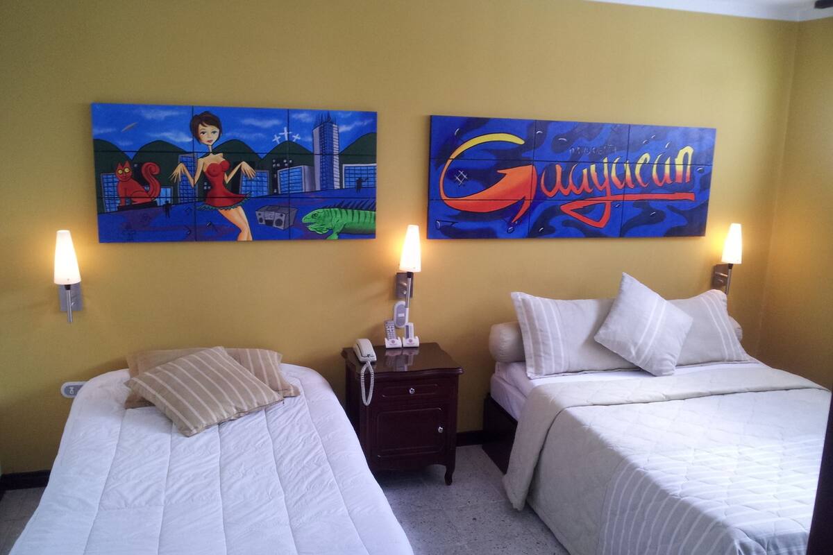 A hotel room with two beds, a nightstand with a phone, and two wall-mounted lamps.