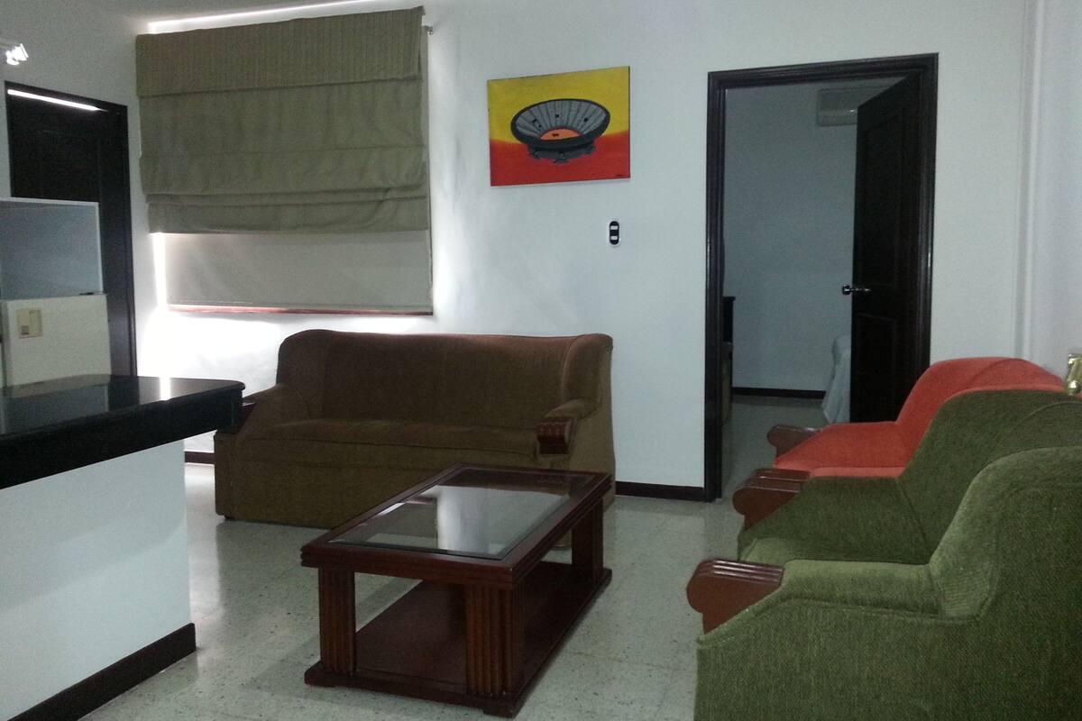 A living room with a brown sofa, a green sofa, a glass coffee table, and a painting on the wall.