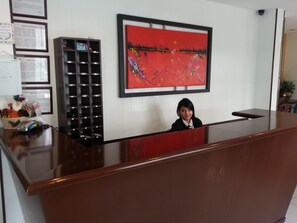A reception desk with a red abstract painting above it, a bulletin board with notices, and a plant in the corner.