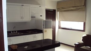 Una cocina compacta con armarios blancos, encimera negra y ventana con persianas.