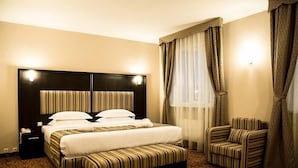 A hotel room with a large bed, a bedside table, a chair, and a window with curtains.