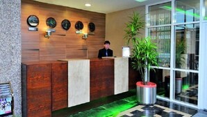 A reception desk with a wooden panel design, a receptionist, and a large potted plant.