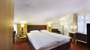 Una camera d'albergo con un letto matrimoniale, comodini, una scrivania con una sedia, una televisione e una finestra con tende.