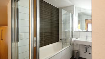 Un baño moderno con ducha de vidrio, una bañera blanca y un lavamanos con espejo.