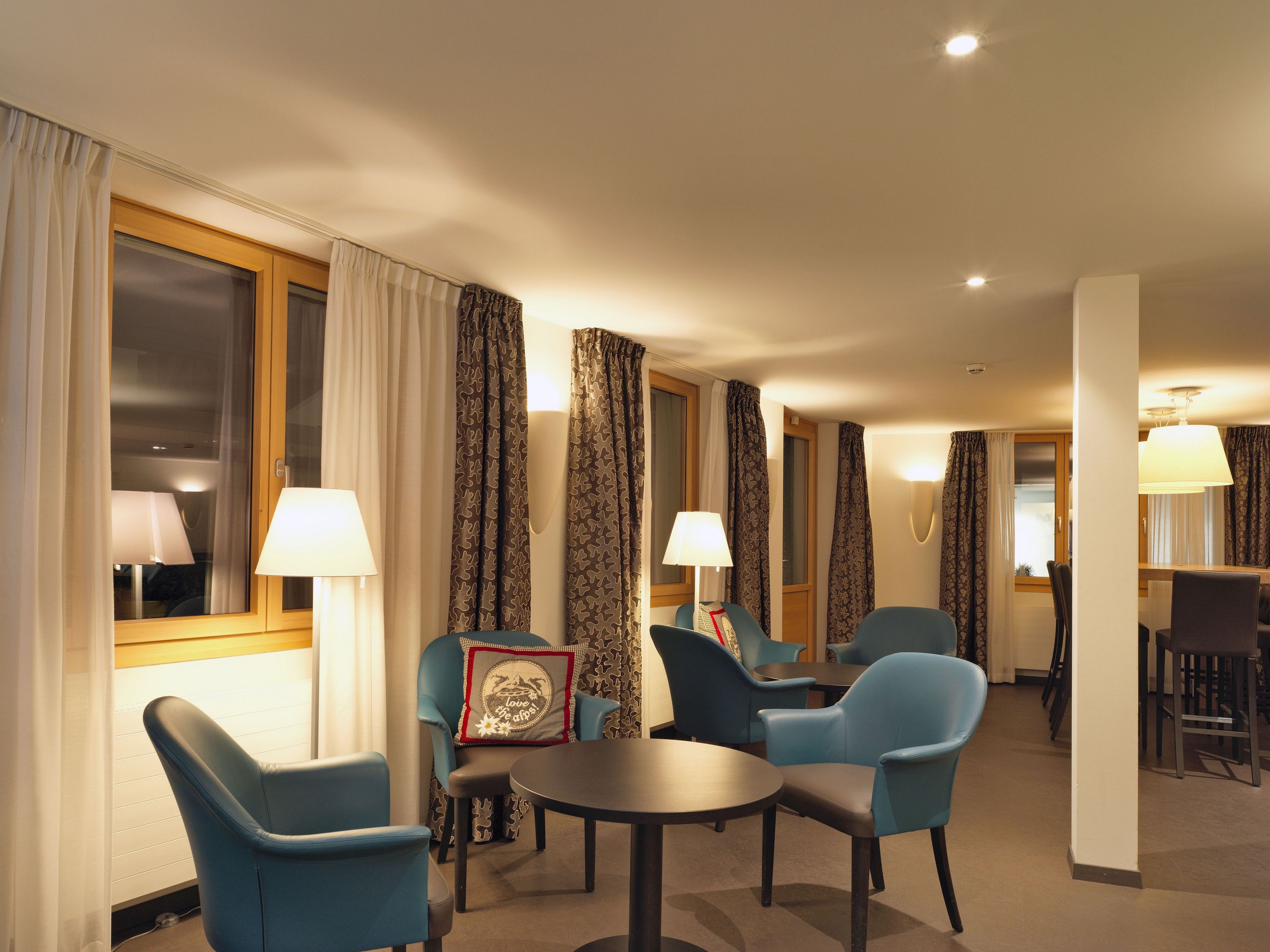 Habitación de hotel con comedor, sillas azules, una mesa redonda y cortinas estampadas.