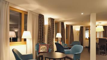 Habitación de hotel con comedor, sillas azules, una mesa redonda y cortinas estampadas.