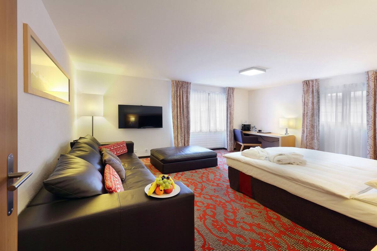 A hotel room with a bed, a sofa, a desk, a TV, and a fruit plate.