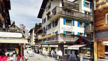 Un hôtel à plusieurs étages doté de balcons ornés de fleurs, une pharmacie et un magasin de montres Tissot.