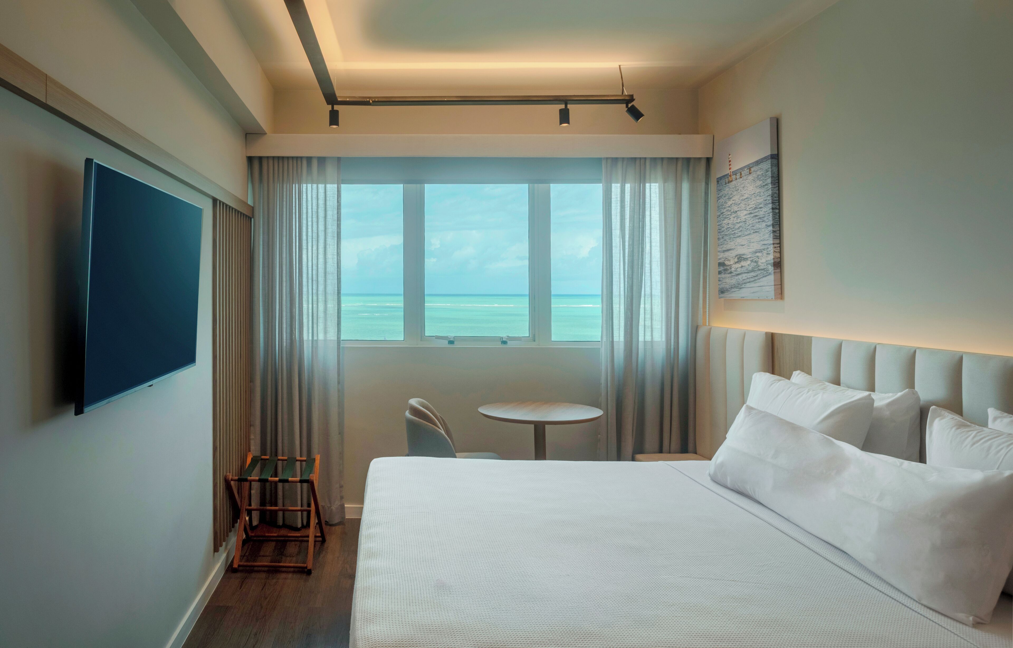 Hotelkamer met een groot bed, een klein tafeltje, een stoel, een televisie en een raam met uitzicht op zee.
