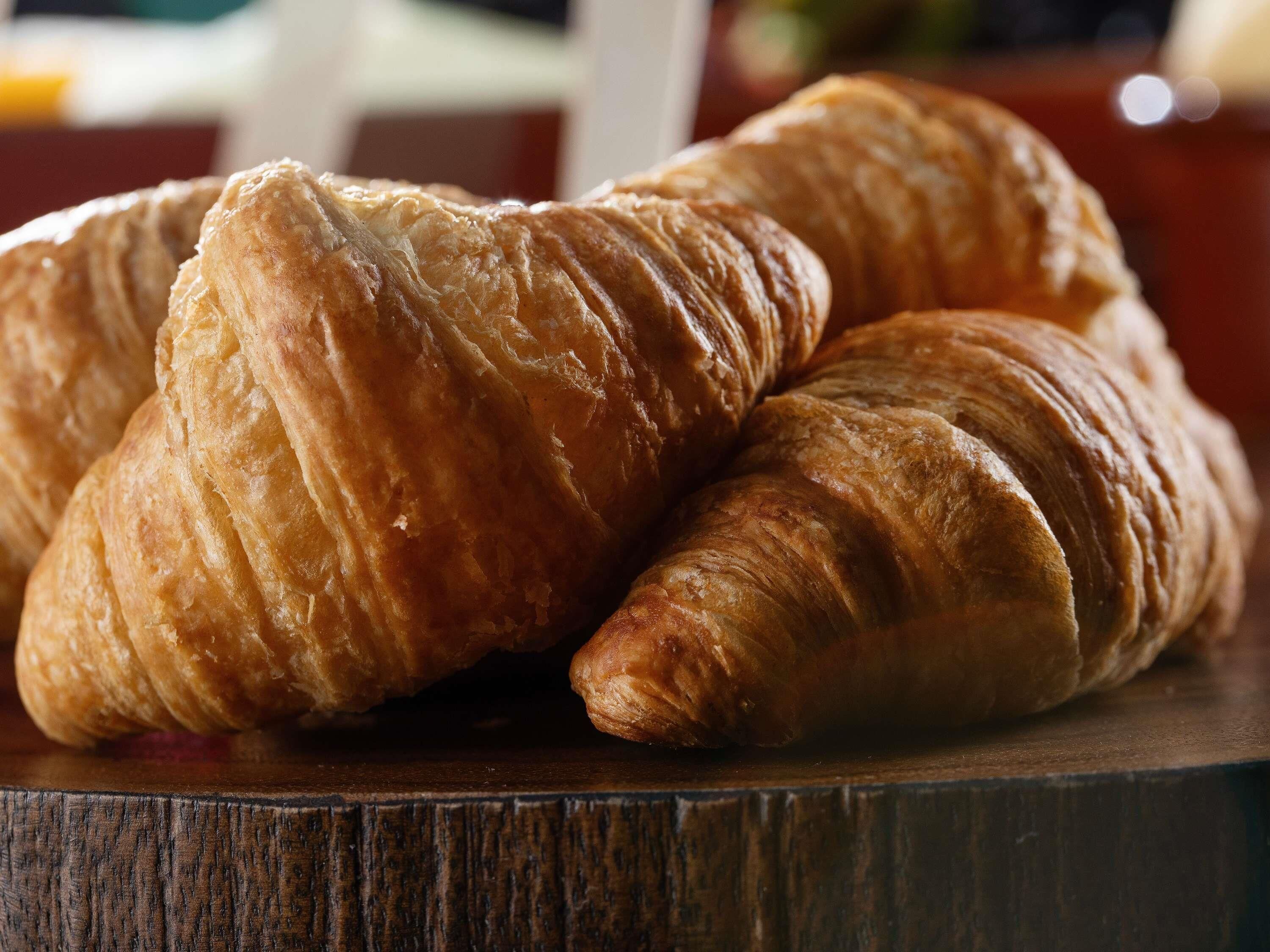 Zwei Croissants auf einer Holztischplatte.