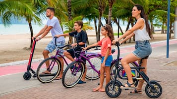 Un grupo de personas montando en bicicleta por un camino pavimentado, con palmeras y una playa al fondo.