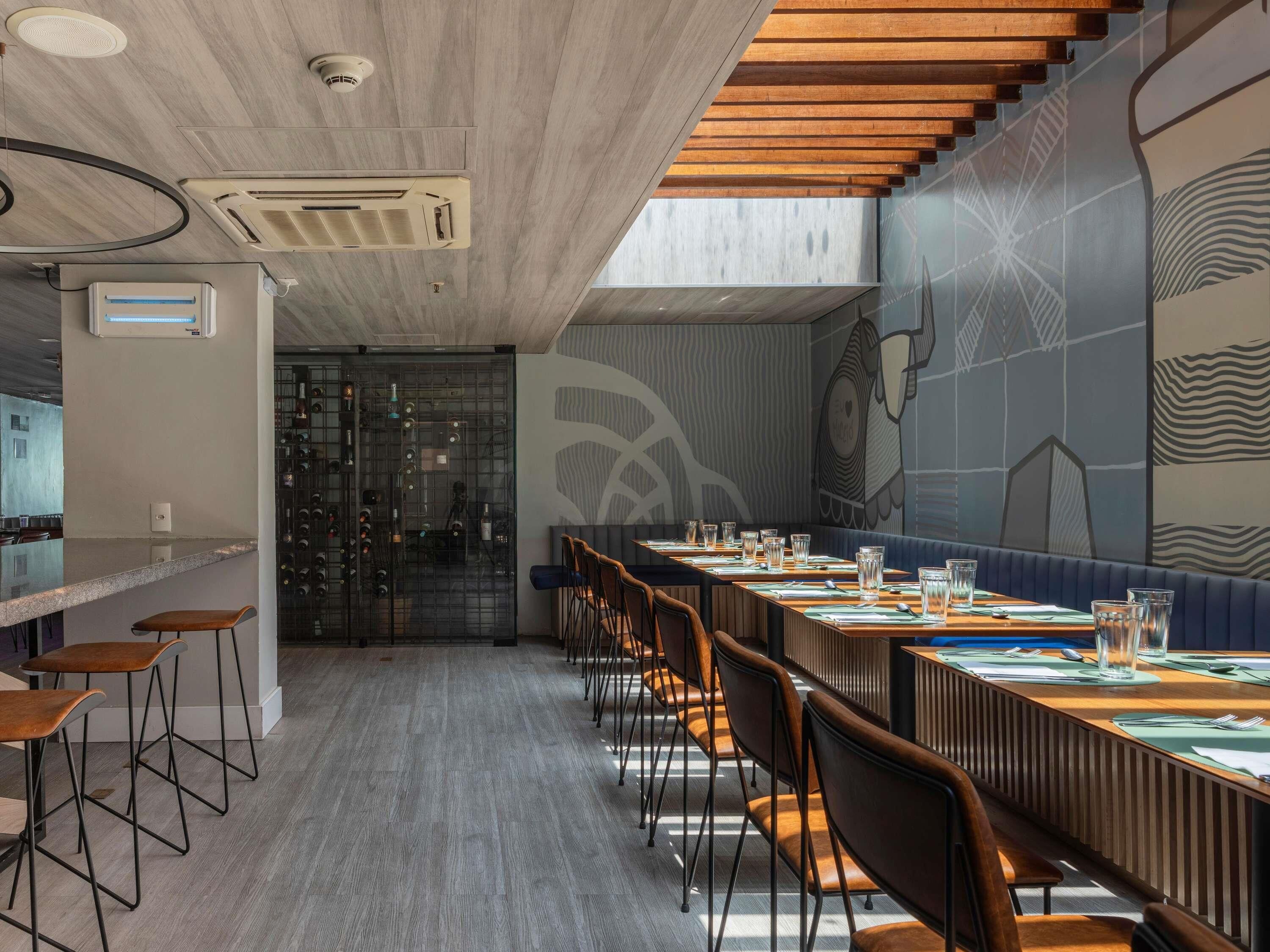 A modern restaurant with a long counter, bar stools, and a mural on the wall.