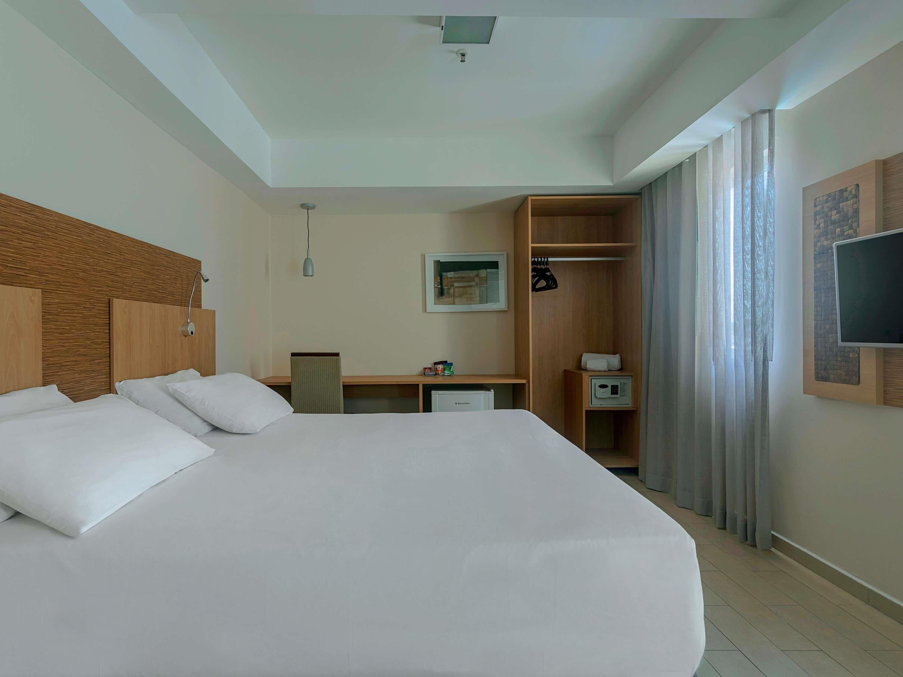 A hotel room with a large bed, a desk, a wardrobe, a television, and a shower.
