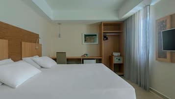 A hotel room with a large bed, a desk, a wardrobe, a television, and a shower.