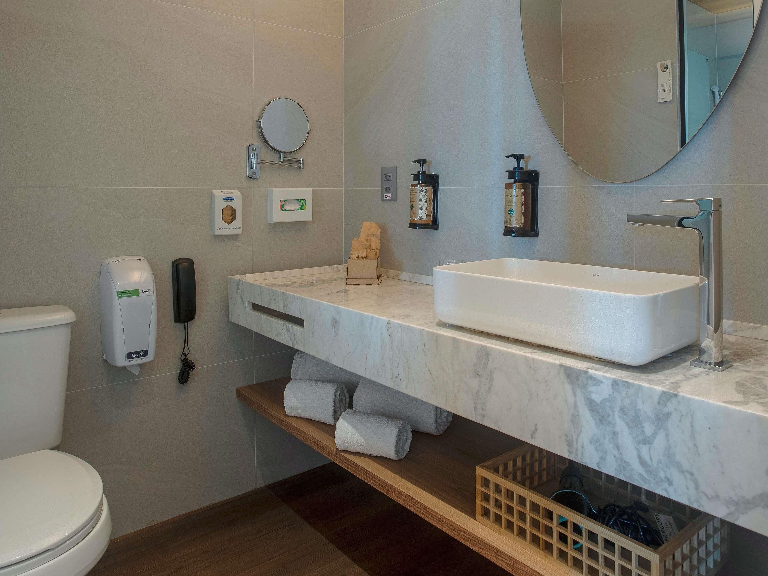 A modern bathroom with a white sink, a mirror, a toilet, and a shelf with towels.