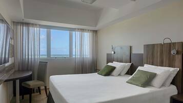A hotel room with a large bed, two bedside tables, a desk with a chair, and a large window with curtains.