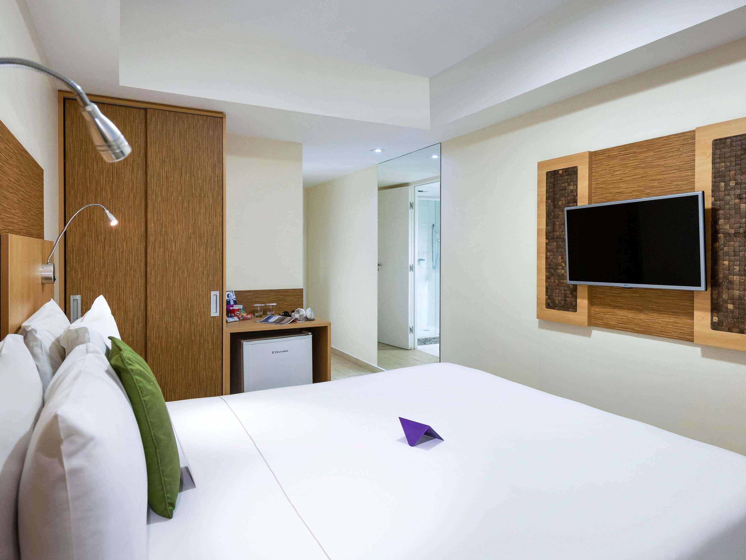 Une chambre d’hôtel avec un lit, un bureau, une télévision et un miroir.