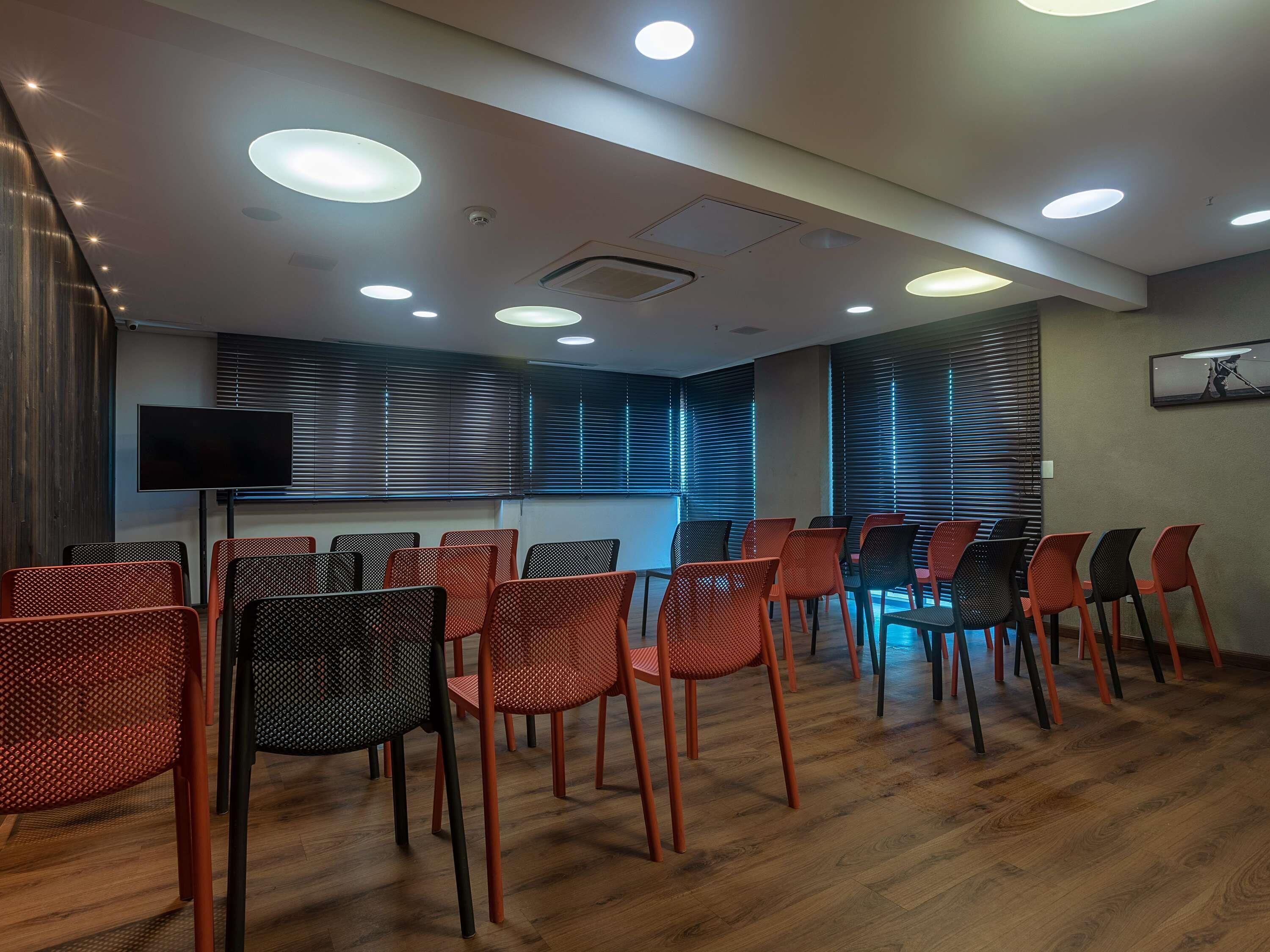 Un salón de conferencias con una pantalla grande, filas de sillas y luces en el techo.