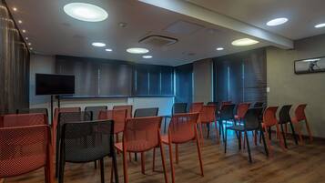 Un salón de conferencias con una pantalla grande, filas de sillas y luces en el techo.