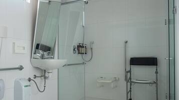 Un baño moderno con cabina de ducha de vidrio, un banco accesible para sillas de ruedas, un inodoro con toalla y un lavabo con espejo.