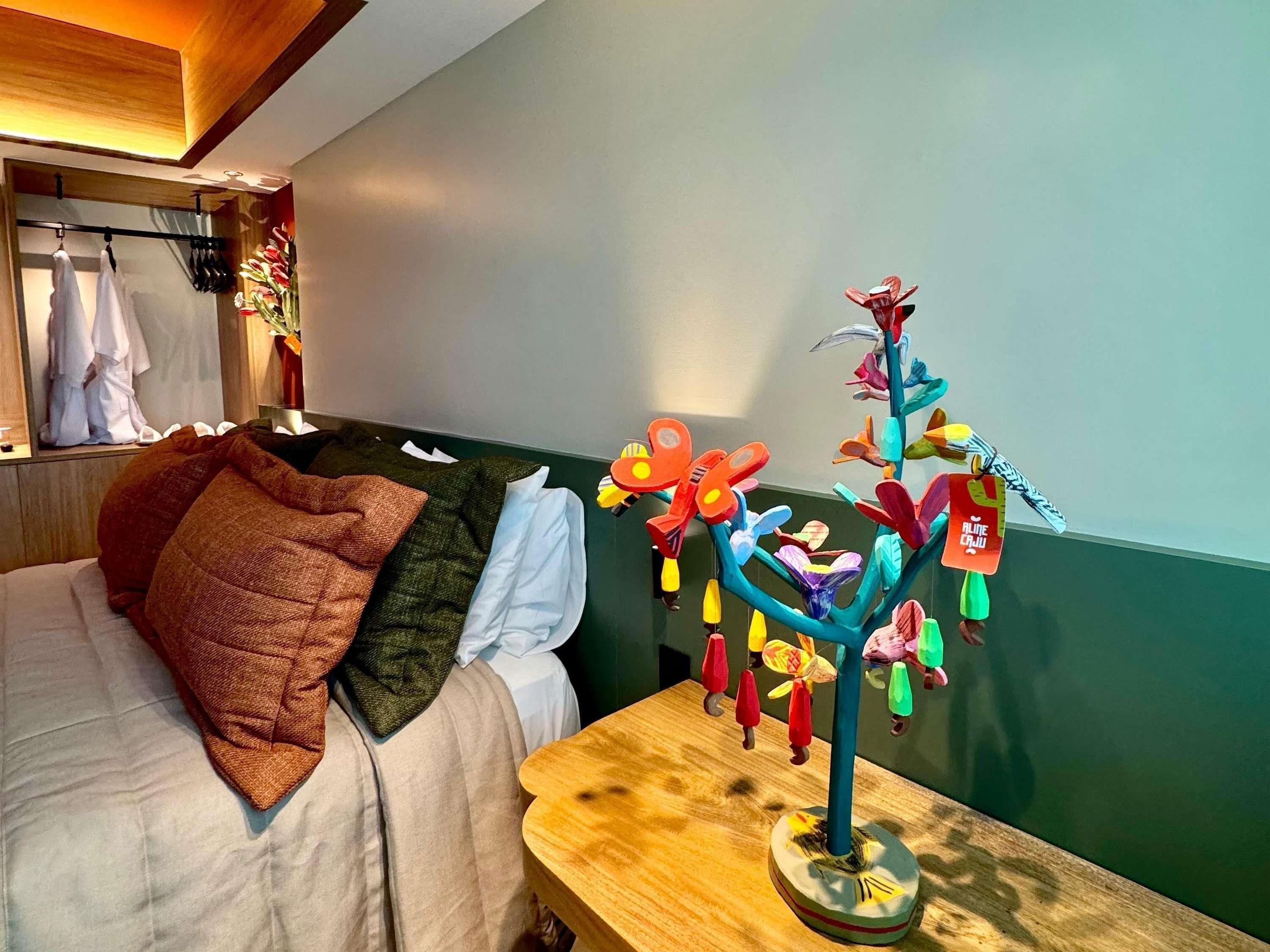 Un dormitorio con una cama, almohadas, una mesita de noche de madera y un móvil de mariposas de colores.