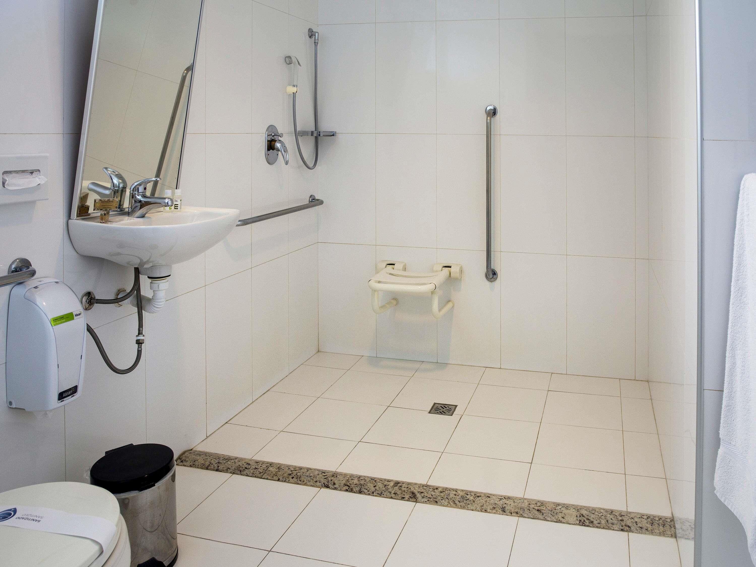 A bathroom with a sink, mirror, shower, grab bars, and a toilet.