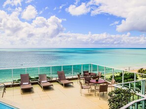 A poolside area with lounge chairs and tables, overlooking a clear blue sea and a beach. - Mercure Maceio Pajucara Hotel (Maceió)