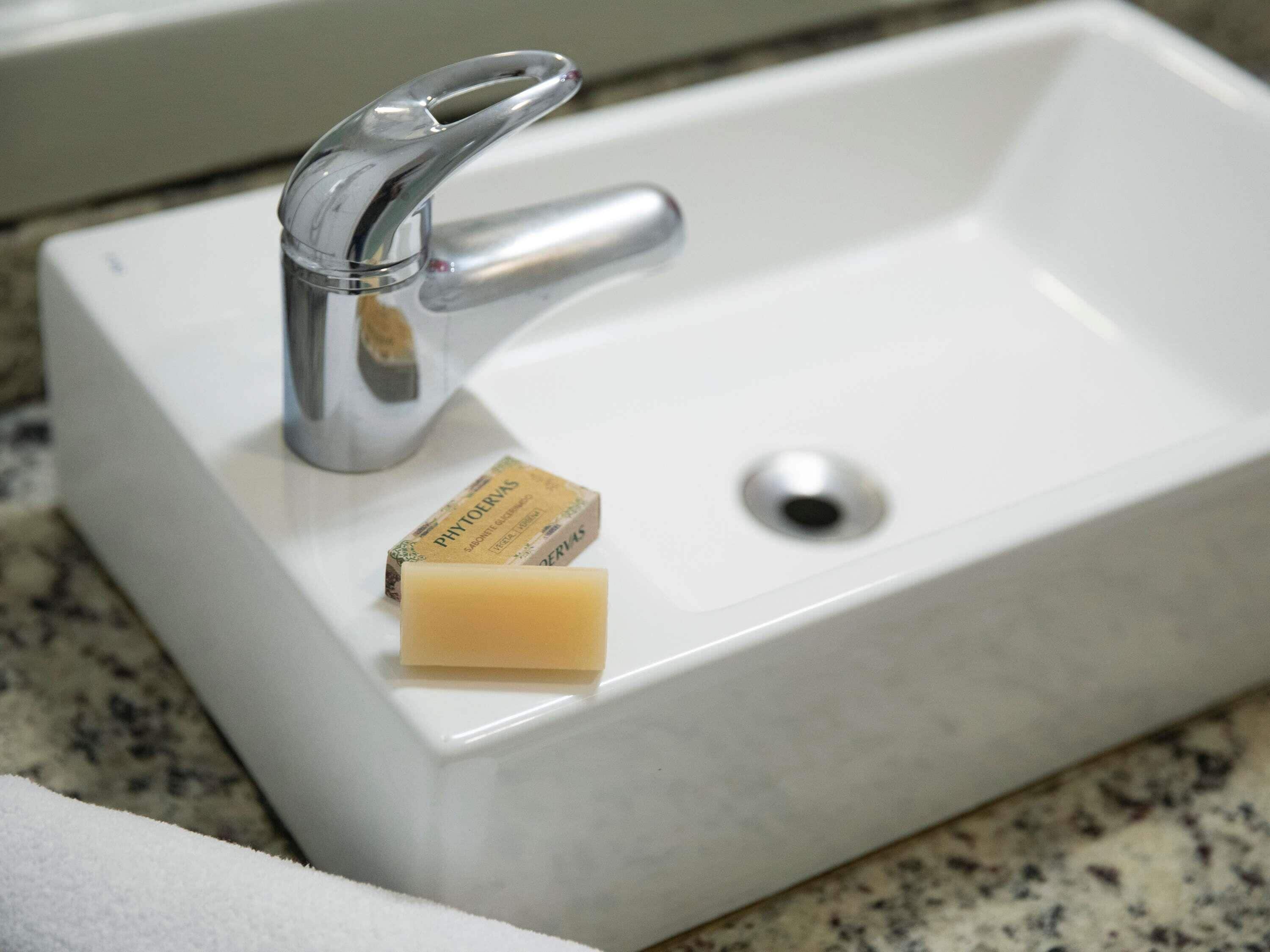 Un lavabo blanc pour la salle de bain, avec un robinet chromé, un savon et un bouchon d’évier.