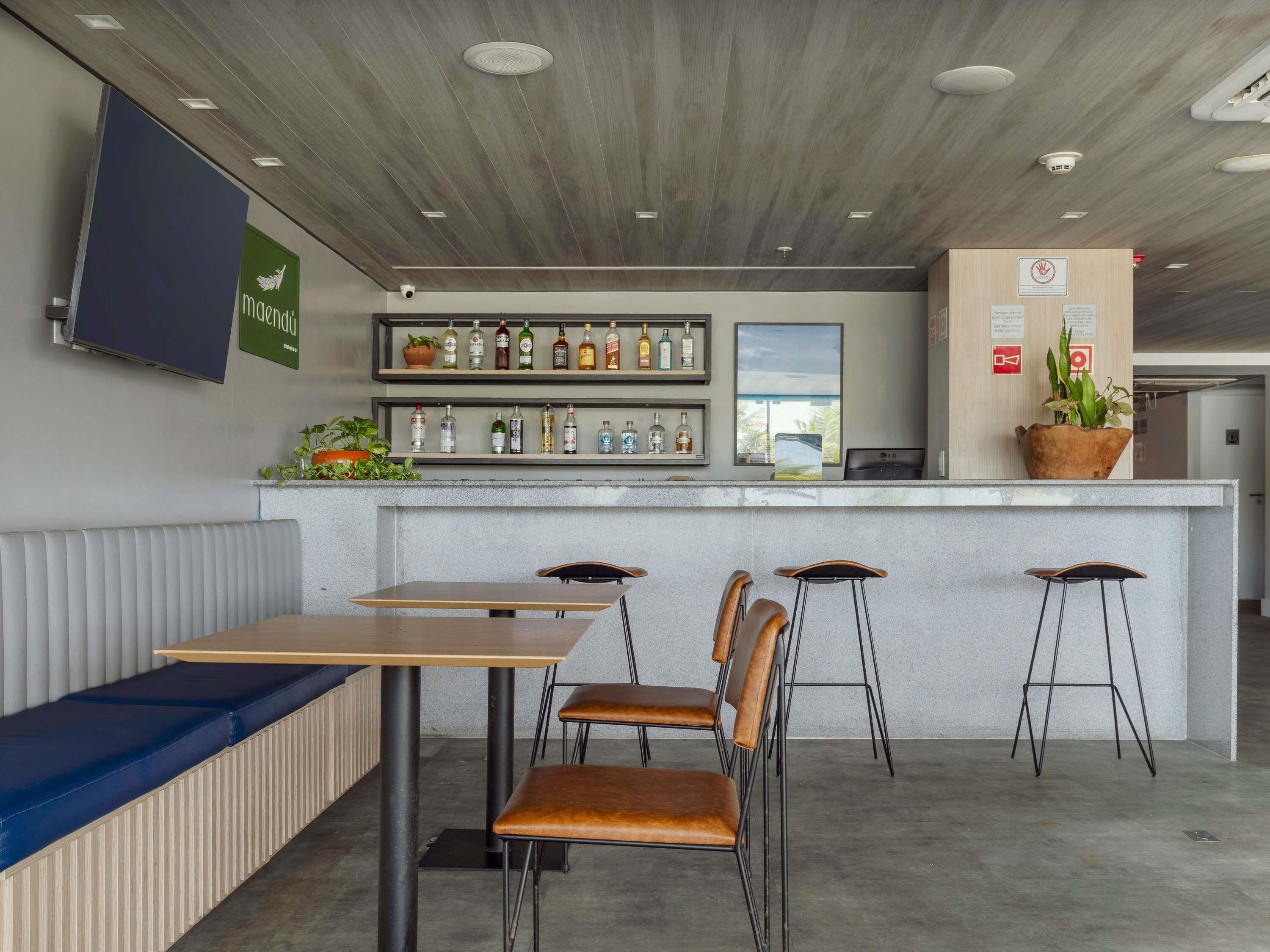 A bar area with stools, a counter with bottles, a TV, and a seating area with benches.