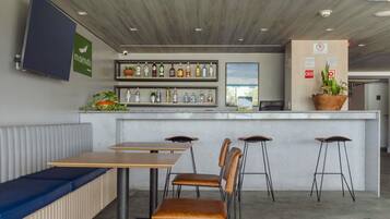 A bar area with stools, a counter with bottles, a TV, and a seating area with benches.