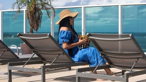 A woman sitting on a lounge chair by a pool with a view of the ocean. - Mercure Maceio Pajucara Hotel (Maceió)