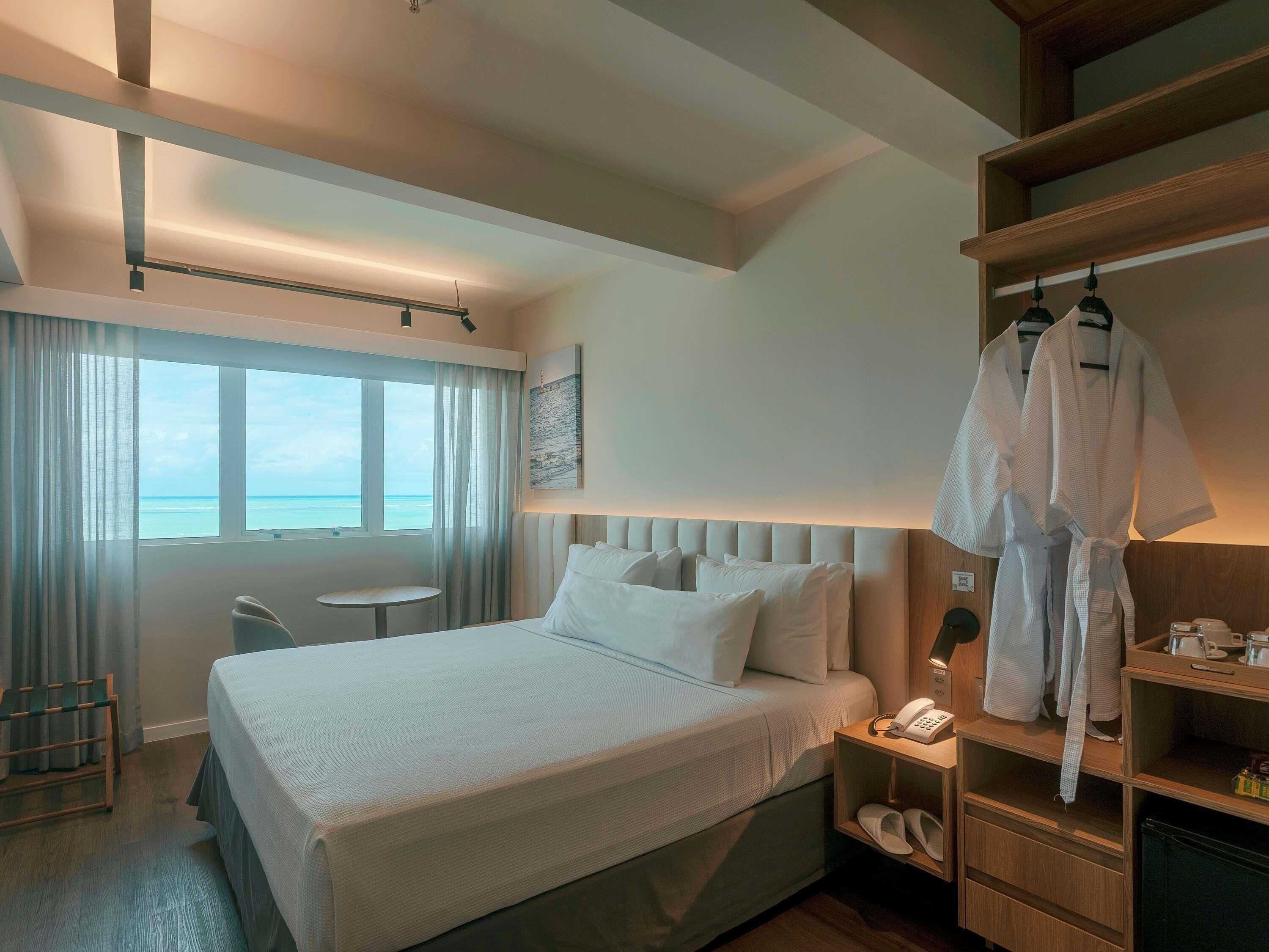 A hotel room with a bed, bedside table, and a view of the ocean.