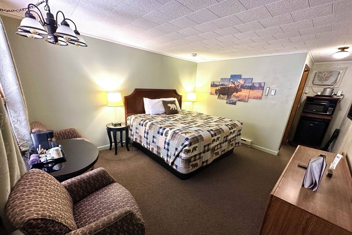 Habitación de hotel con cama, escritorio, silla, lámpara y microondas.