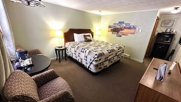 A hotel room with a bed, a desk, a chair, a lamp, and a microwave.