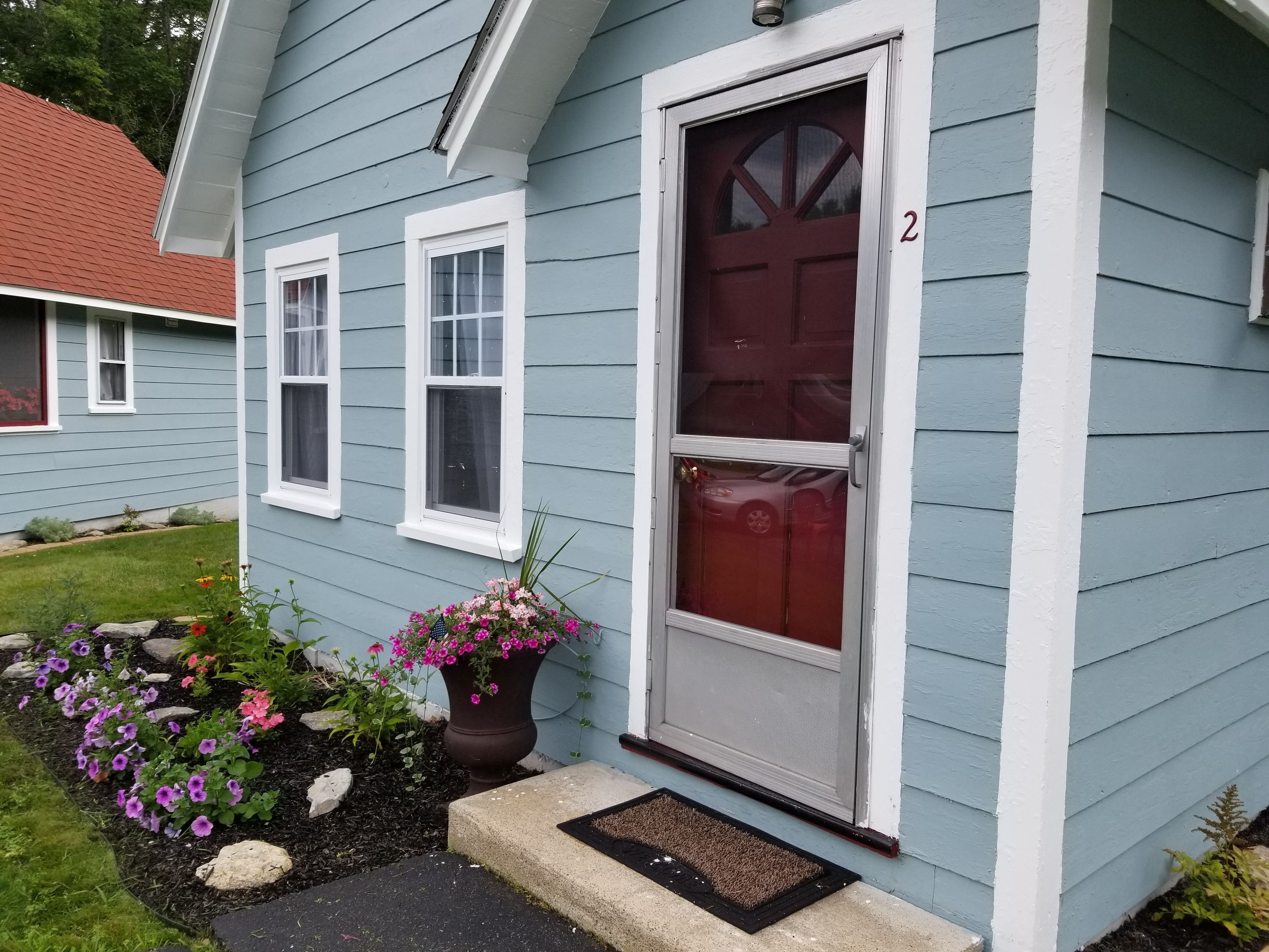 A house with a red door, white-framed windows, and a number '2' on the wall.