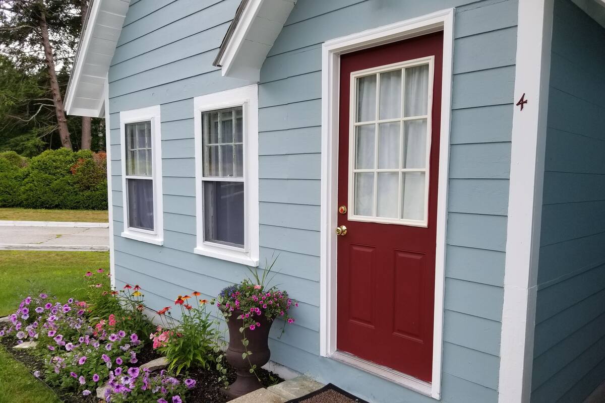 Una casa con puerta roja, dos ventanas y un jardín delantero lleno de flores.