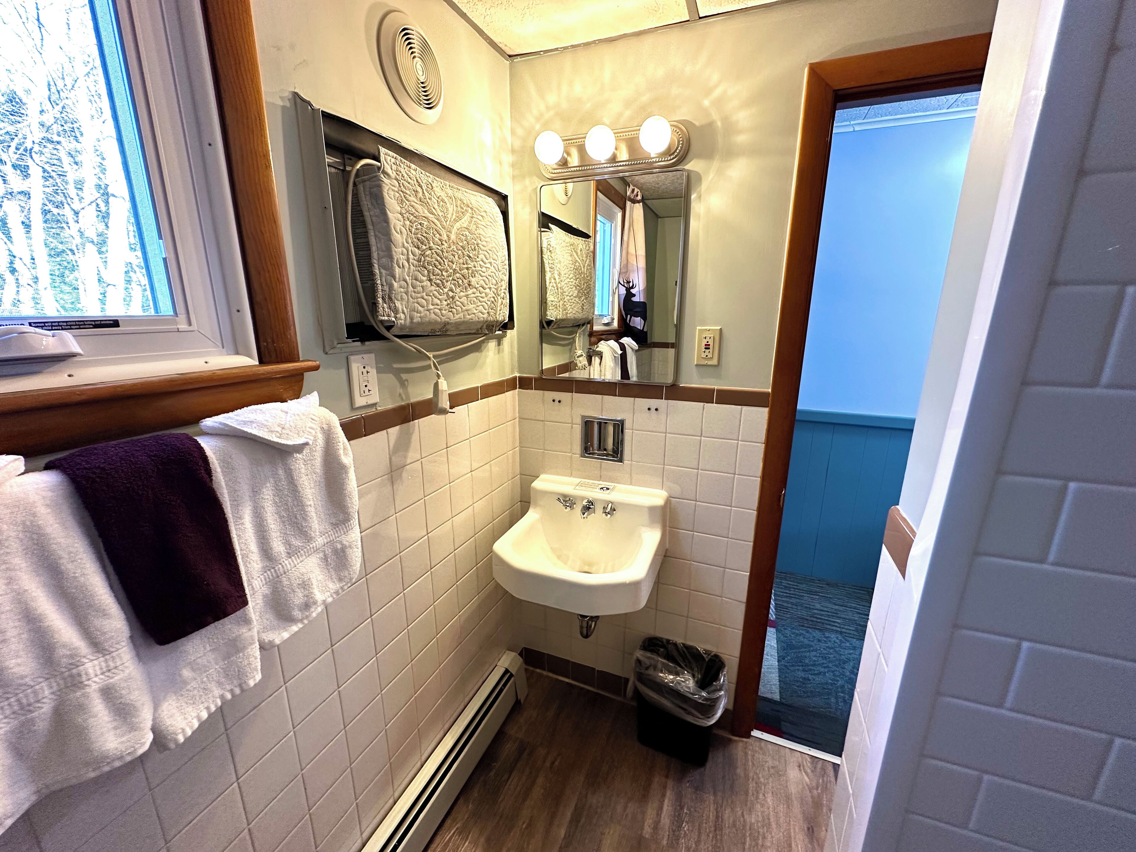 A bathroom with a sink, mirror, towel rack, and a window with blinds.