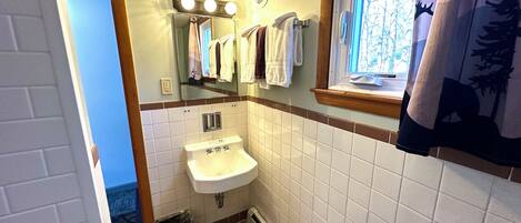 A bathroom with a sink, mirror, and window. There are towels hanging on the wall and a trash can.