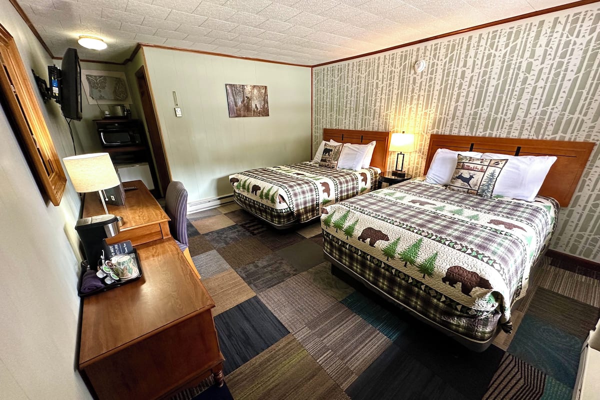 Una habitación de hotel con dos camas, un escritorio, una silla, un televisor y una lámpara.