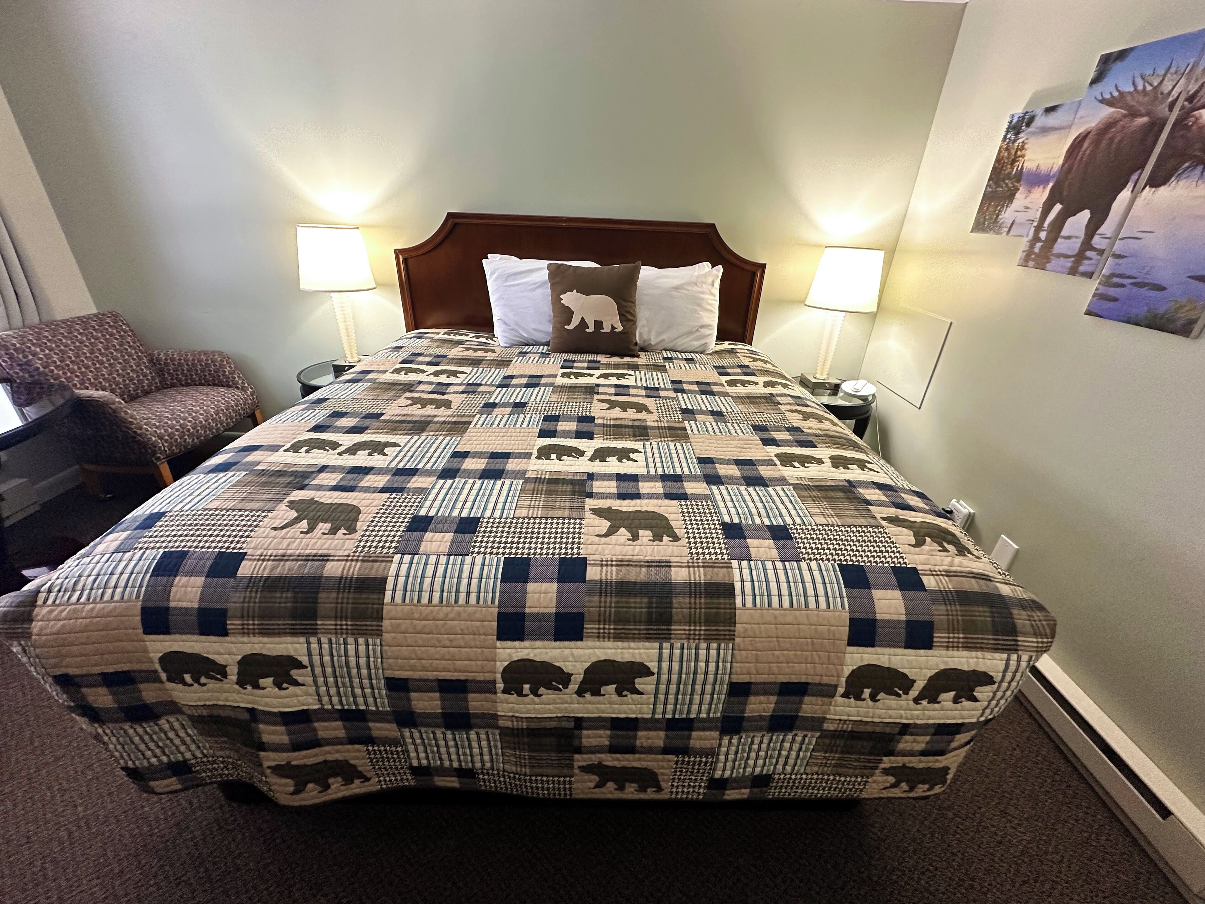Ein Bett mit einem gewölften Muster von Bären, zwei Nachttischlampen, ein Stuhl und ein Wandbild.